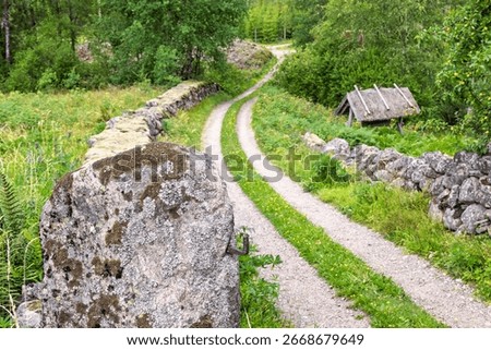 Boulder as a gatepost by an old winding dirt road with stone walls in the country