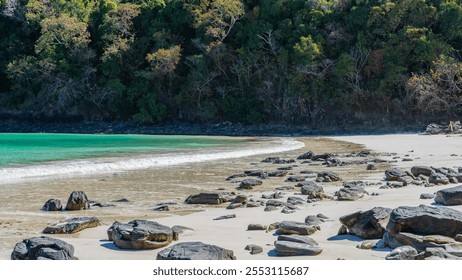 Boulders are scattered on the sandy beach. The waves of the turquoise ocean foam and spread over the sand. Green vegetation on the coastal cliffs. Madagascar. Nosy Iranja    - Powered by Shutterstock