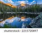 Boulders surround the calm water of Chipmunk Lake reflecting Ypsilon Mountain and Mount Chiquita lit by morning light in Rocky Mountain National Park, Colorado.