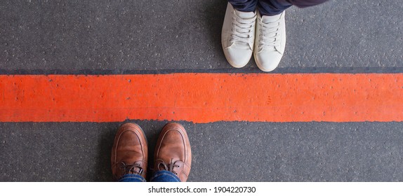 Boundary, quarantine, social distancing and differences concept. Man and woman standing opposite of each other, divided by a thick red line. Wide angle view, copy space.