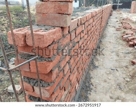 Boundary wall under construction using red bricks and cement mortar at rural site, showing traditional bricklaying process and step-by-step layering of bricks for compound wall building