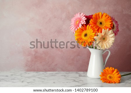 Bouquet of beautiful bright gerbera flowers in vase on marble table against color background