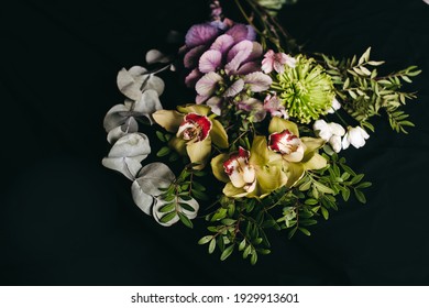 The bouquet of beautiful mixed flowers on a black background. Chrysanthemum green, yellow orchid flower, white rose and green leaves. Unusual original fresh bouquet. Dark still life composition.