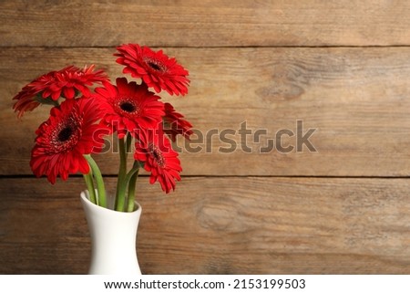 Bouquet of beautiful red gerbera flowers in ceramic vase on wooden background. Space for text