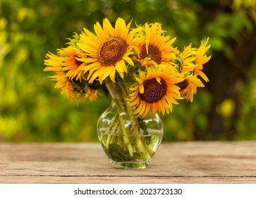 bouquet of beautiful yellow sunflower flowers in a glass vase on an old rustic wooden table in the garden - Powered by Shutterstock