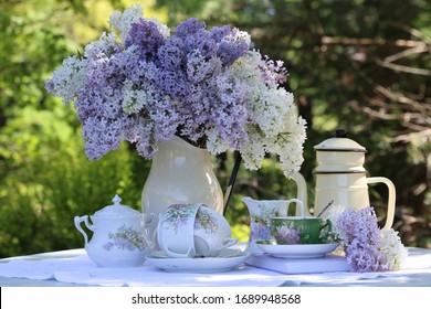 Bouquet, branches of white and purple lilac in enamel pitcher, coffeepot, porcelain, china tea cup on wooden aged weathered table, floral scene in garden, spring sunny day, vintage style - Shutterstock ID 1689948568