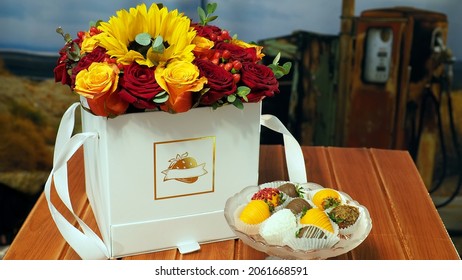 a bouquet of bright red and yellow flowers in a white box and handmade candies on a crystal plate