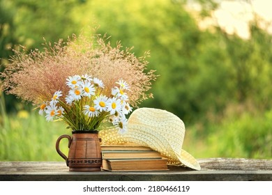 Bouquet with Chamomile flowers, books and braided hat on table in sunny garden. Harmony, peaceful mood, relax time. summer season concept. Rustic composition
