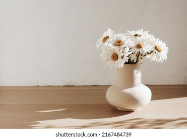 bouquet of daisies flowers in a ceramic vase on beige wooden table near a white textured wall. Copy space.Minimal Scandinavian interior. Neutral trendy colors interior decoration .