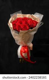 Bouquet of dark red roses in floral paper with red ribbon isolated on black background