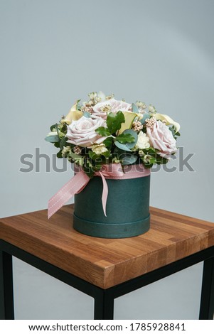Bouquet of flowers in green hat box on wooden chair on a light background. Rosa, calla, astrantia, eucalyptus, ozotamnus.