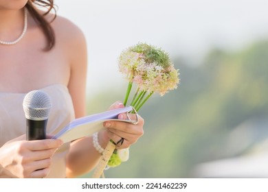 A bouquet of flowers in the hands of a female host, holding a microphone, waiting for the schedule to report the order of the event - Powered by Shutterstock