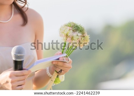 A bouquet of flowers in the hands of a female host, holding a microphone, waiting for the schedule to report the order of the event