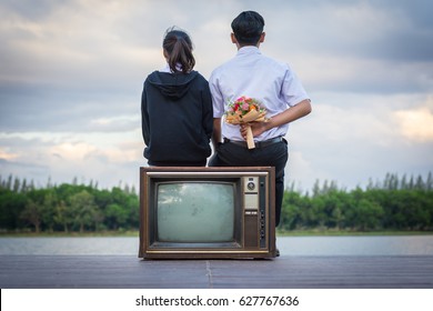 A Bouquet Of Flowers In The Hands Of A Young Man Hidden Behind. While Watching The View On The Old TV.