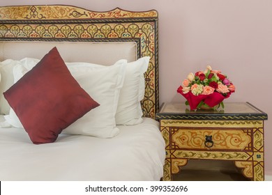 A Bouquet Of Flowers On A Bedside Table Next To A Bed With A Painted Headboard