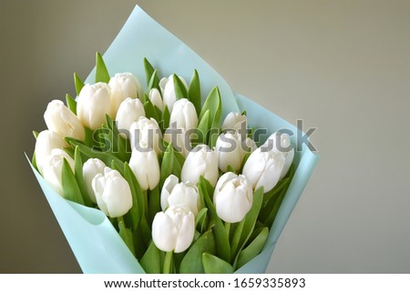 Bouquet of fresh white tulips with mint decoration paper on blurred green background. Gift for romantic date. Beautiful white tulips. Tender spring flowers. Bunch of tulips for Mother’s Day