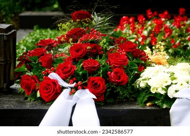 a bouquet of funeral flowers from red roses with white mourning bow on a grave after a funeral - Powered by Shutterstock