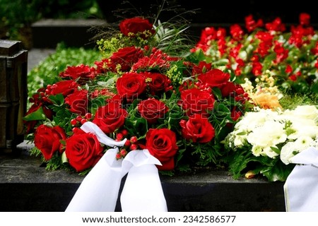 a bouquet of funeral flowers from red roses with white mourning bow on a grave after a funeral