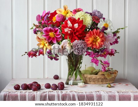 bouquet of garden flowers in a glass vase, plums and apples, still life in a rustic interior. asters and dahlias.
