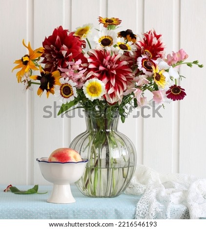 A bouquet of garden flowers in a glass vase and nectarine on the table.