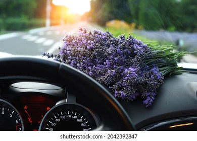 A Bouquet Of Lavender On The Torpedo Of A Car And A View Of The Road From Behind The Wheel Of The Car. Artistic Photo With Soft Focus 

