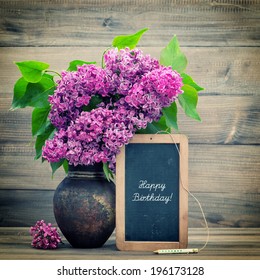 bouquet of lilac flowers on wooden background. blackboard with sample text Happy Birthday! retro style toned picture