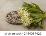 Bouquet  lilies of the valley (Convallaria majalis) on  basket  on a gray table. Symbol of the first of May in France "Lily of the Valley Day" (Le jour du Muguet)