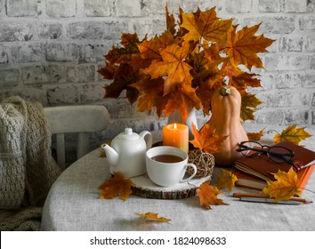 Bouquet of maple leaves, pumpkin, hot tea, lighted candle on the kitchen table.Warm cozy autumn interior                     