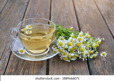 Bouquet of Matricaria chamomilla and cup of chamomile tea on a wooden table close-up. Concept of a healthy lifestyle.