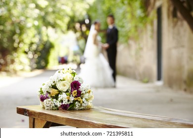 bouquet on wooden bench with bride and groom in the background, focus on the flowers. - Powered by Shutterstock