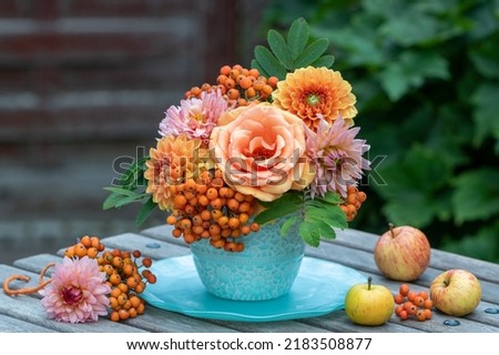 bouquet of orange rose, dahlias and rowan berries in vase in garden