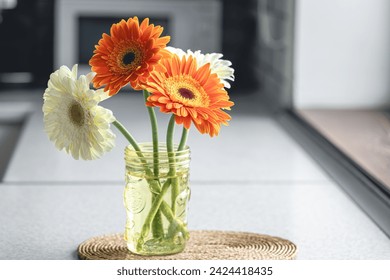 A bouquet of orange and white gerberas in a vase in a kitchen interior.