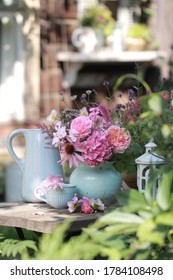 A bouquet of pink flowers in a blue ceramic vase and other dishes on the table in the village garden