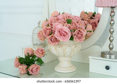 Bouquet of pink roses in vase on white boudoir table with oval mirror. Detail of the interior of the room with female boudoir