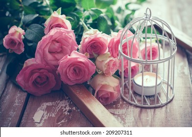 Bouquet of pink roses, wooden frame and a burning candle in a white decorative bird cage on old board background, vintage decor and color tinting - Powered by Shutterstock