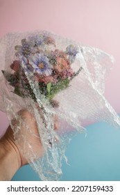 A bouquet of plastic flowers covered by bubble plastic wrap in  a left hand with pastel colors background. Plastic pollution creative minimal concept. Environment, environmental problems.   - Shutterstock ID 2207159433