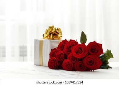 A bouquet of red roses and a gift box on the table in the interior. Love confession. Valentine's day celebration - Powered by Shutterstock