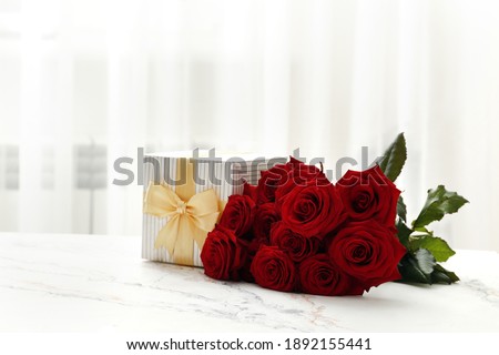 A bouquet of red roses and a gift box on the table in the interior. Love confession. Valentine's day celebration