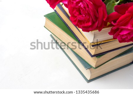 A bouquet of red roses on a pile of books on a light stone background. Concept love of literature and romance novels