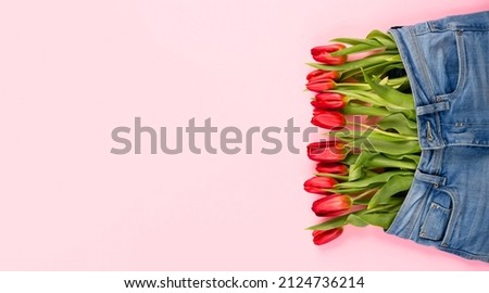 A bouquet of red tulips peeks out of pants or shorts on a pink background. The concept of a healthy diet, a beautiful body, youth, weight loss or losing weight. Top view mockup.