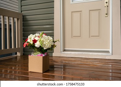 A bouquet of red white flowers in a carton box on a porch doorstep of a house. Surprise contactless delivery of flowers for woman. Delivery to home during quarantine. A pleasant gift. Space for text.