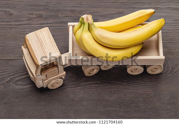  Bouquet of\
ripe bananas in  truck trailer, toy made of wood. Dark wooden\
background, studio shot,\
close-up.