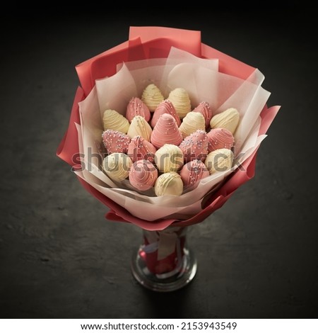A bouquet of ripe strawberries covered with white and pink chocolate stands in a vase on a black background