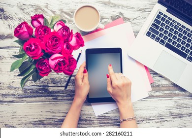 Bouquet Of Roses, Cup Of Coffee, Female Hands With Tablet And Laptop On Old Wooden Table. Top View. Toned Image