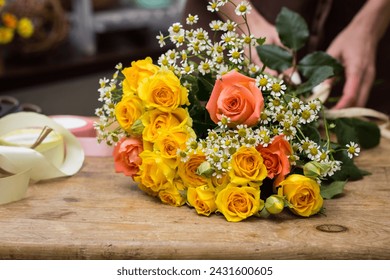 Bouquet of roses and daisies on the table the store close-up.Florist in an apron tying a ribbon on a bouquet.The process of creating a bouquet.Education and courses in floristry. - Powered by Shutterstock