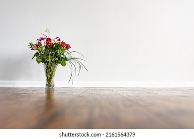 A Bouquet With Roses And Decorative Long Grass Leaves Placed On The Hardwood Floor Of Empty Domestic Room With White Wall