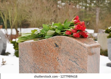 Bouquet of roses on a tombstone of grave on a snowy graveyard in winter 
