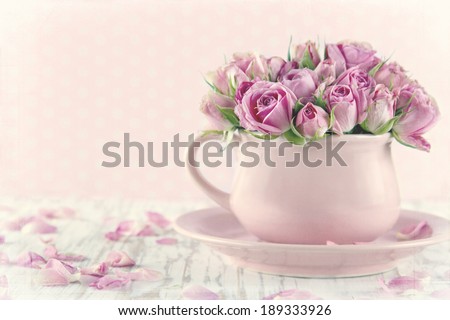 Bouquet of roses in a pink cup on wooden background with vintage textured editing