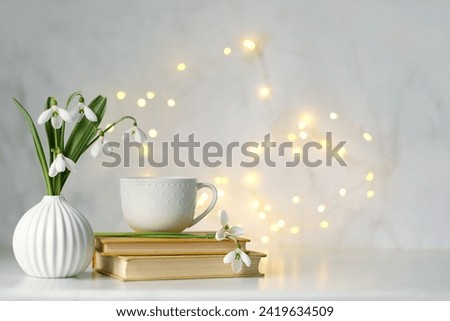 Bouquet of Snowdrop flowers , tea cup and books on table, abstract light background. symbol of spring season. Relaxation, reading time, harmony of nature. template for design