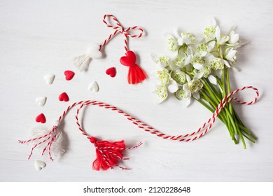 A bouquet of snowdrops flowers, red and white rope with tassels martenitsa, hearts on a wooden background. Postcard for the holiday of March 1